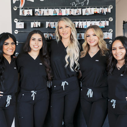Five dental team members in black scrubs smiling together in the office