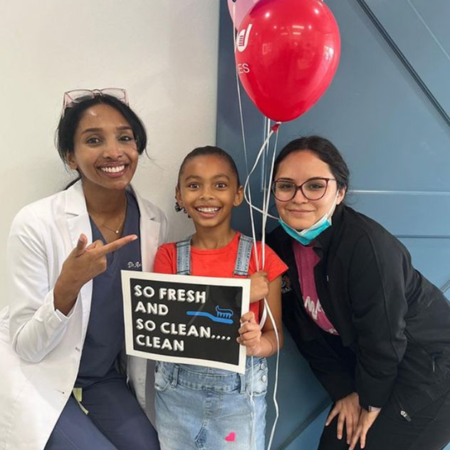 Smiling orthodontist and two kids holding a toothbrush-themed dental health sign